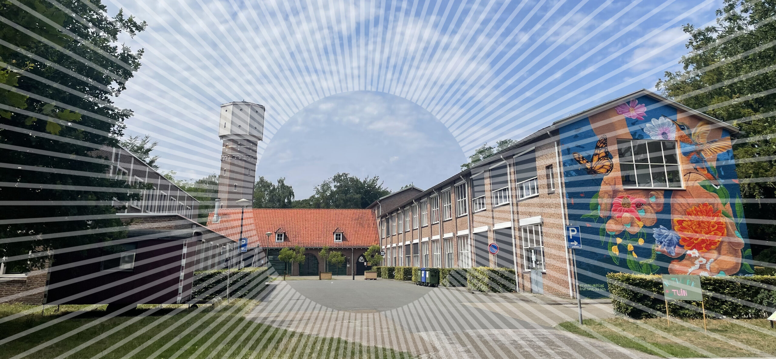 Zicht op een terrein met een karakteristieke watertoren en een kleurrijke muurschildering op een bakstenen gebouw